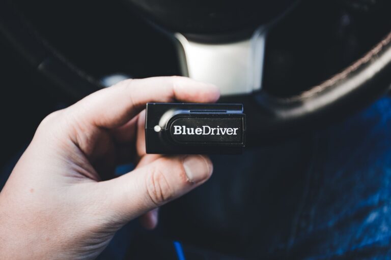 Dłoń trzyma bezprzewodowy tester diagnostyczny BlueDriver w samochodzie